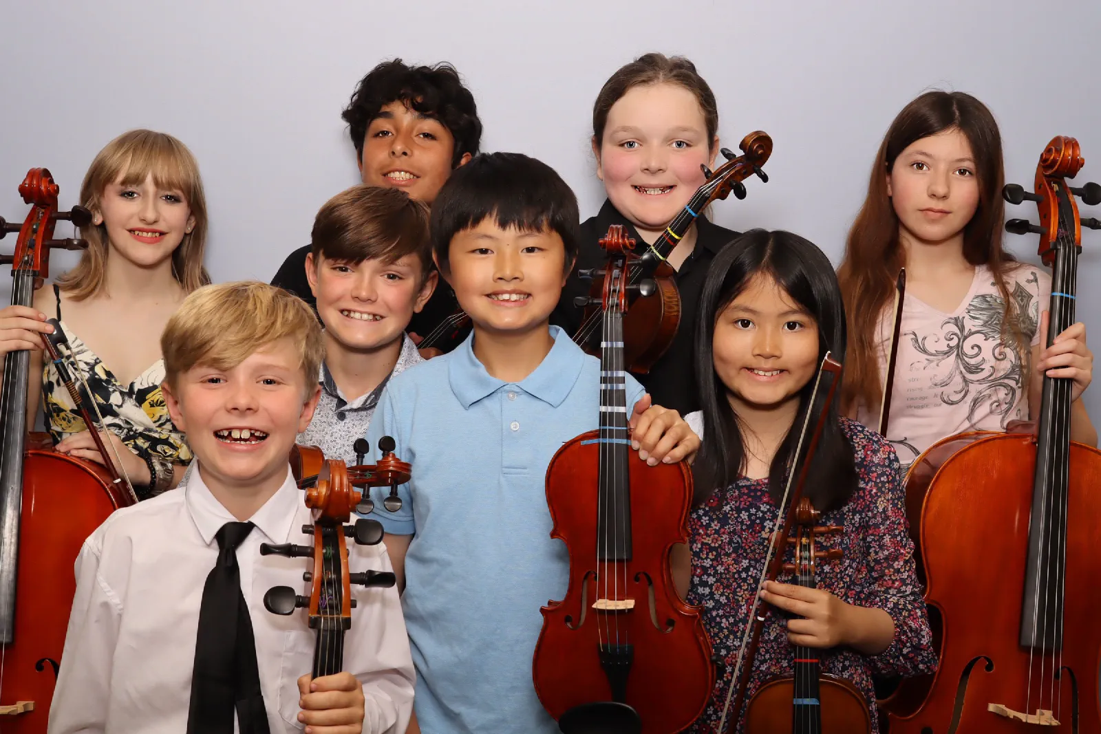 Eight smiling PCYO students holding their violins, violas and cellos