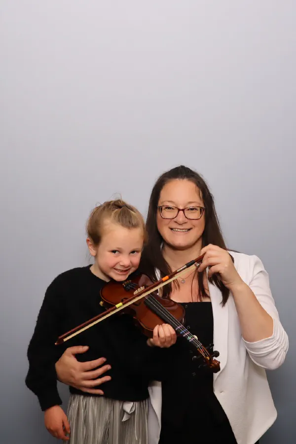 A young Suzuki Sprouts student and her teacher holding a violin together