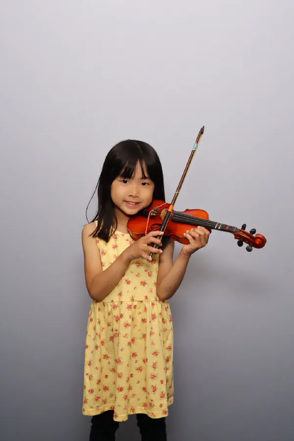 A young girl in a yellow dress playing her violin