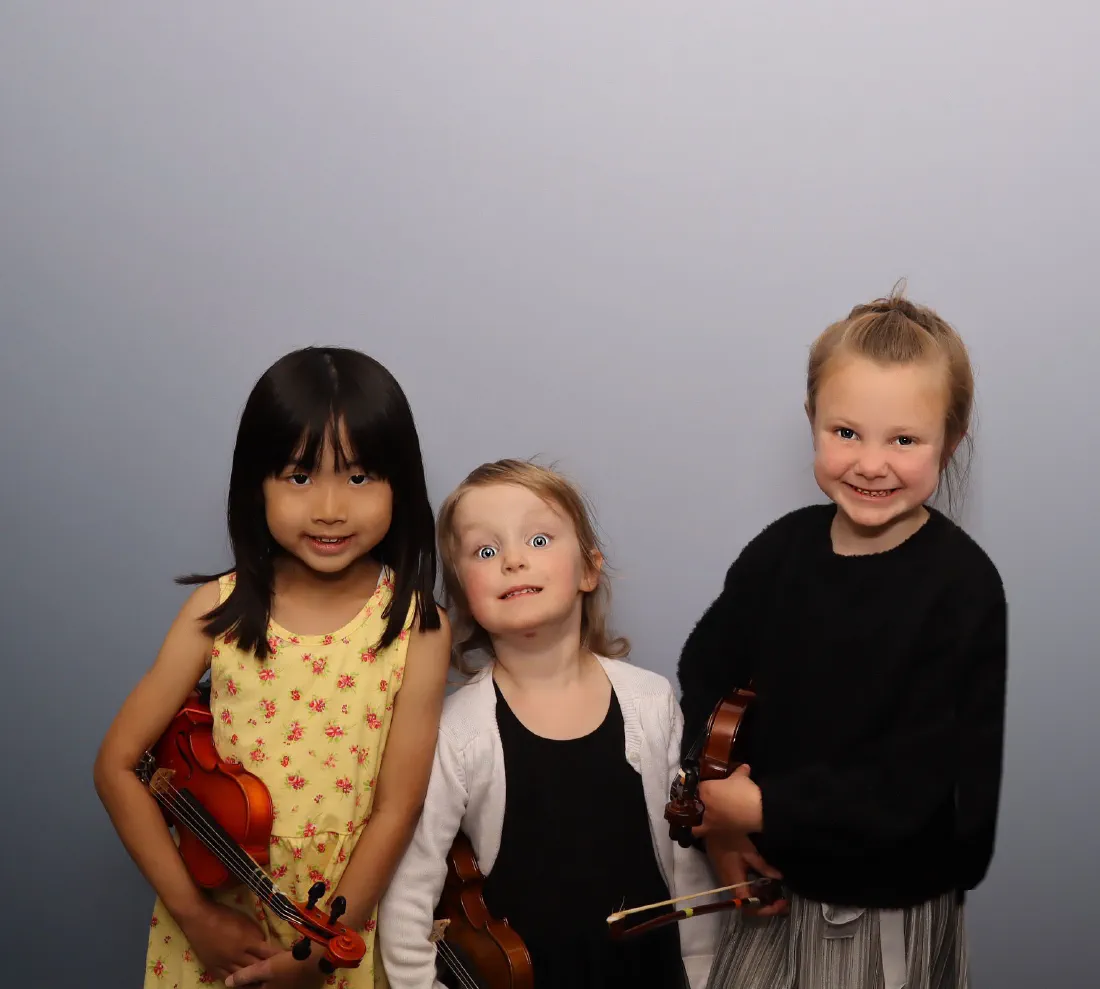 Three young violin students grinning at the camera